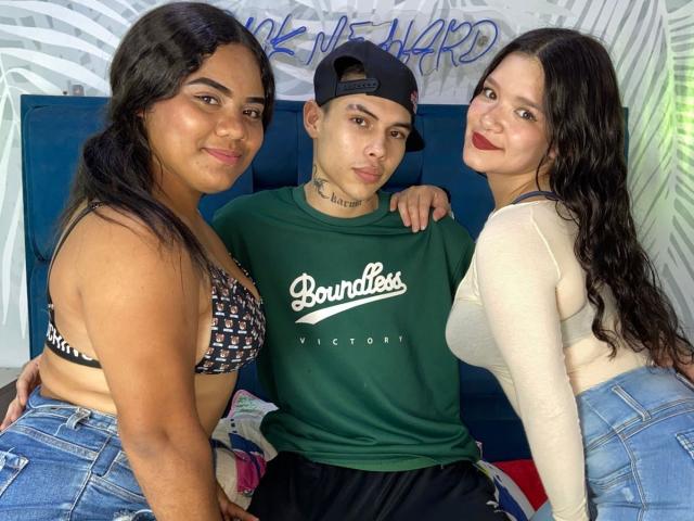 TripleTemptation on left with black hair, patterned bra, and denim shorts; TripleTemptation in center, green t-shirt, black cap; TripleTemptation on right, white top, red lipstick. Sexual tension, close pose, casual setting.