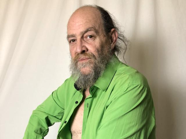 Foto van UmbertoHottie, een oudere man met een kaal hoofd en grijze baard, die een open groene shirt draagt, waardoor zijn borst. Hij heeft een sluw, zelfverzekerde uitdrukking. Ongelooflijk aantrekkelijk..