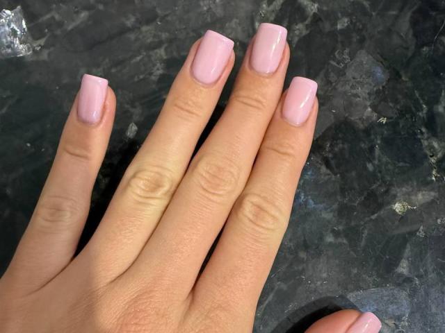 Close-up of JenifferBrown's hand with pink, glossy, square-shaped nail polish on each finger. Skin tone is light. Dark, textured background. Fingers slightly spread, showcasing nails. Fucking smooth and clean look.