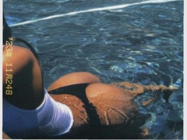 Fotografia ravvicinata della parte inferiore del corpo di SweetNova in una piscina, che mostra gambe abbronzate e muscolose e una canotta bianca. Slip discreti neri, parzialmente visibili. Increspature nell'acqua sullo sfondo. "Incredibilmente attraente"."