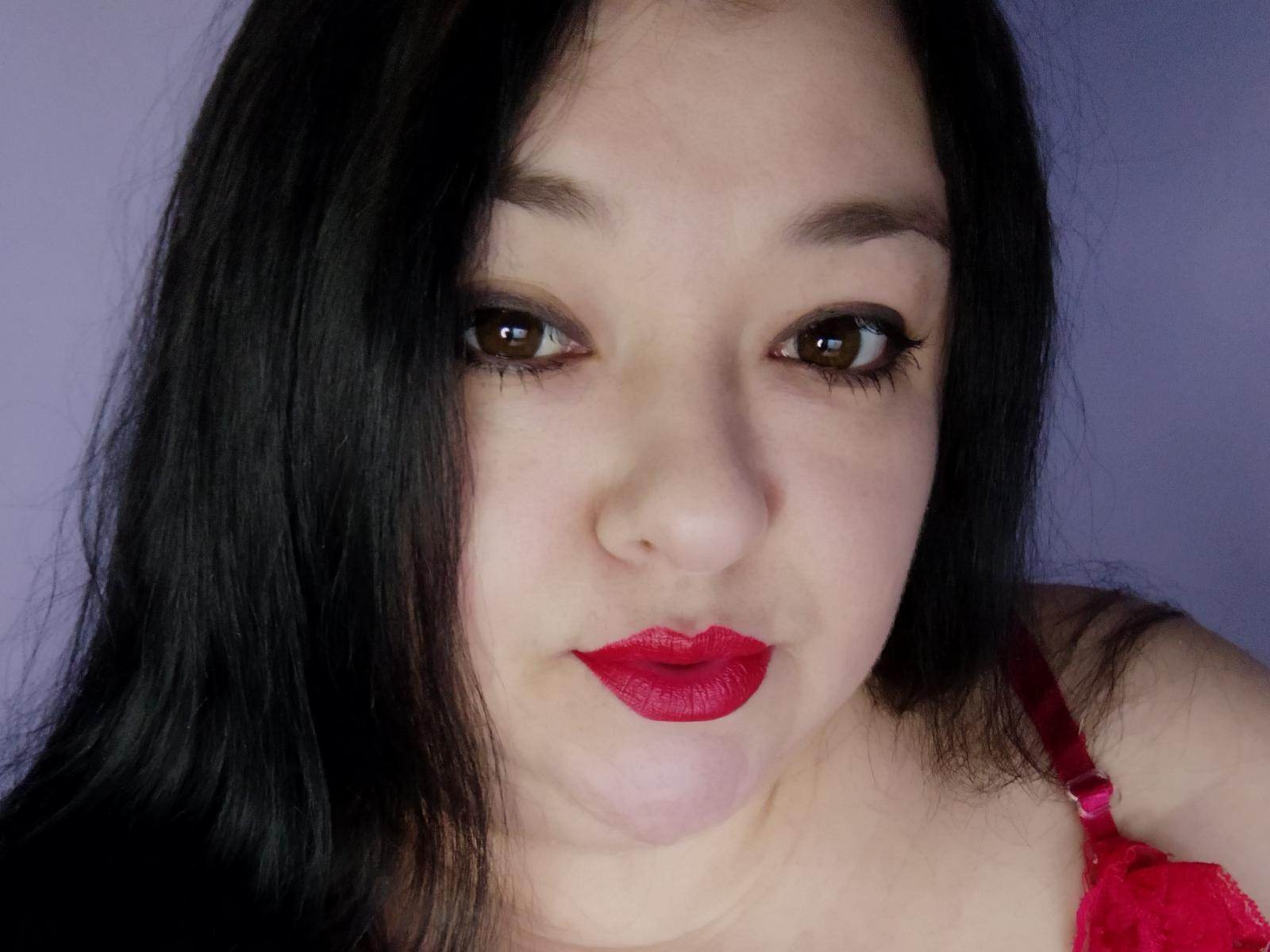 Fotografía de primer plano de FearlessFairy, una mujer asiática con cabello largo y negro, lápiz labial rojo y delineador de ojos oscuro. Ella lleva un sujetador rojo, su expresión es ligeramente sensual, los labios ligeramente entreabiertos..