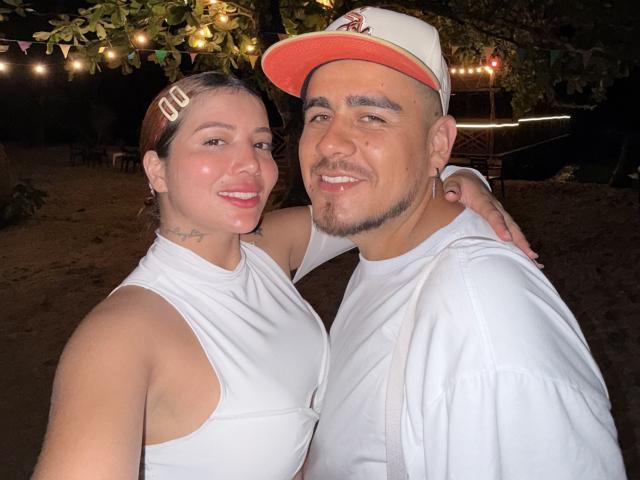 Angeline et Michael, une femme charmante aux cheveux foncés portant un débardeur blanc, et un homme barbu en chemise blanche et casquette, debout, très proches, souriant, tension sexuelle, décor extérieur nocturne..