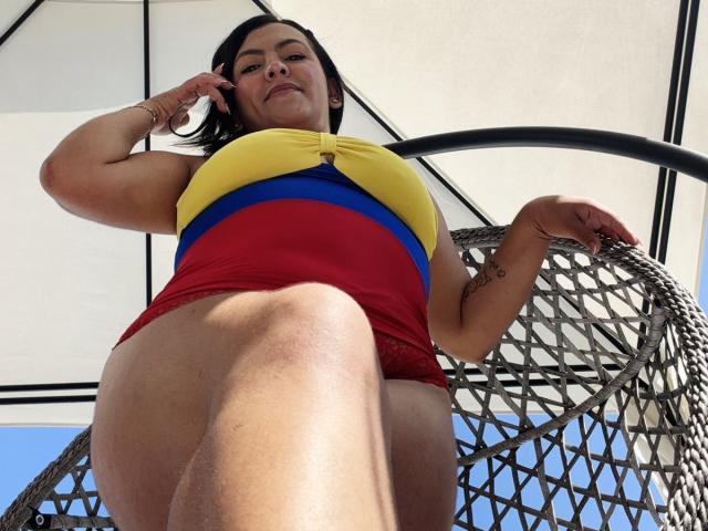 ScarlettOxford, toma desde un ángulo bajo, vistiendo una blusa amarilla y pantalones cortos rojos, reclinada en una silla de red, con las piernas separadas, con el clítoris visible. a través de pantalones cortos, mirada intensa, la luz del sol proyectando sombras, pose provocativa, colores llamativos..