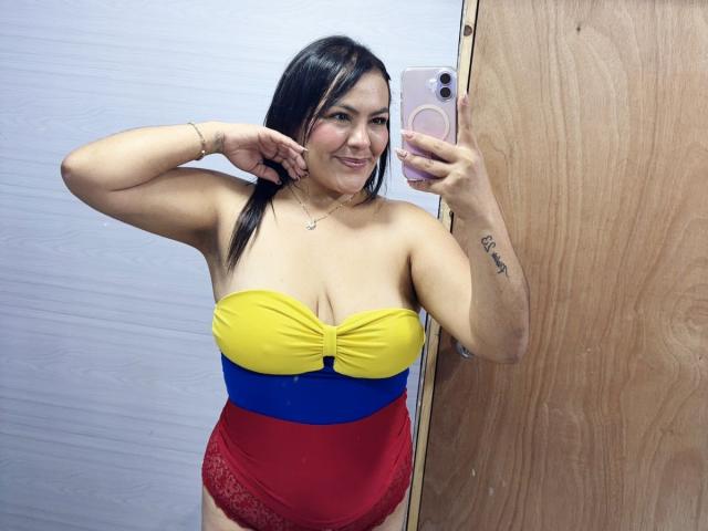 ScarlettOxford, sonriendo en un selfie frente al espejo, lleva un top amarillo sin tirantes con una banda azul y roja, ropa interior de encaje roja y color marrón. cabello, tatuaje en el brazo derecho, sosteniendo un teléfono en la mano derecha. Muy atractivo..
