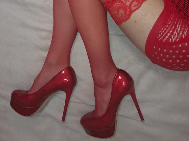 Primo piano delle gambe di Amberia, con calze rosse trasparenti e tacchi alti rossi lucidi. Amberia indossa biancheria intima rossa a pois. Le cosce di Amberia sono leggermente divaricate, creando una tensione sessuale..