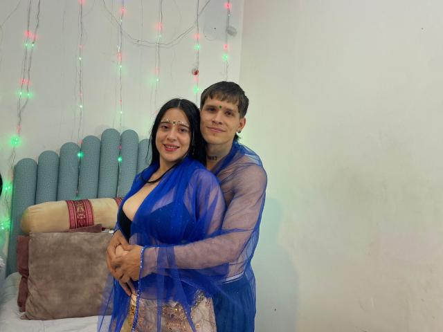 AnjaliRohan and a man in a blue saree and matching shawl, standing close, he's grabbing her waist, colorful string lights in background, wrapped gift on table, sexual tension.