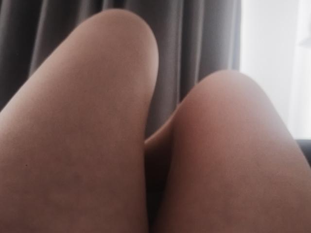 Close-up photo of SusanMonroy's bare legs, thighs pressed together, soft skin, slight shadows, natural light from window, dark curtain in background. Sexual tension, suggestive pose, focus on intimate angle.