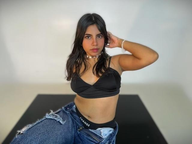 Fotografia de CelesteMorel, com cabelos longos e pretos, vestindo um sutiã preto e calças jeans abertas, revelando roupa íntima preta. com o texto "Vince". Ela está posando de forma sedutora, com a mão no cabelo, e com um olhar intenso..