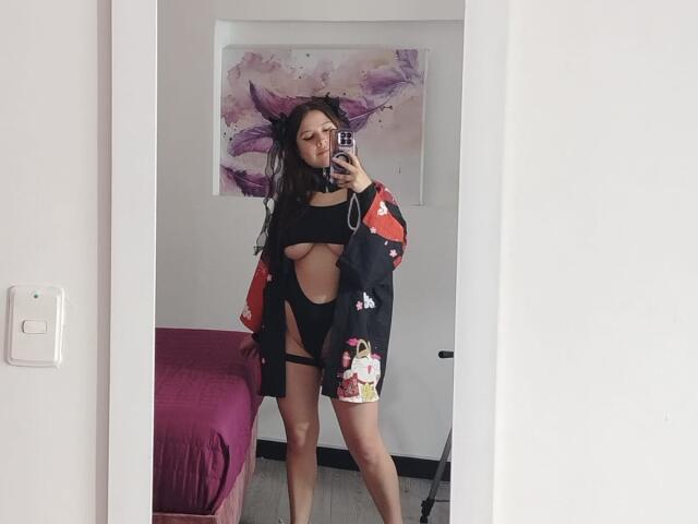 MelaniBecker takes a mirror selfie, wearing a black cut-out top and shorts, with a black jacket featuring red and white details. Long, messy hair, purple abstract art in background. Fucking sexy.