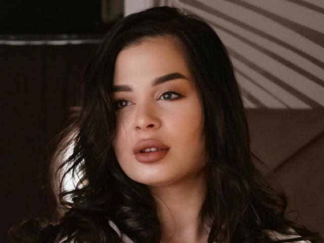 Fotografía de primer plano de LoraIvone con cabello negro largo y ondulado, piel clara y labios carnosos. Ella mira directamente a la cámara con la boca ligeramente abierta, creando una expresión sensual y provocativa..