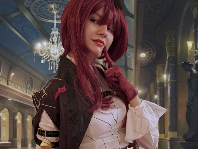 LinaVeritas, com cabelo ruivo, vestida com um traje preto e branco, luvas marrons, dedo na bochecha, e um candelabro. teto ornamentado ao fundo, sorriso discreto, pose confiante, tensão sexual, clima da comunidade de cosplay..