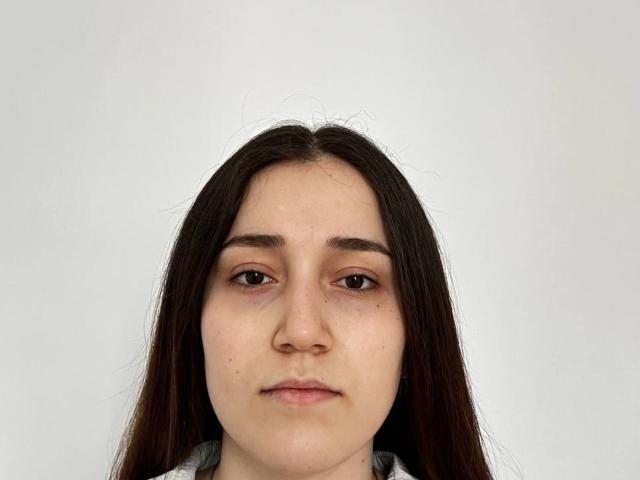 Fotografia di Glennis Mimozo con lunghi capelli castani lisci, pelle chiara e occhi marroni. Espressione neutra, leggero sorriso. Centrato su uno sfondo bianco uniforme. I bordi grigi incorniciano l'immagine..