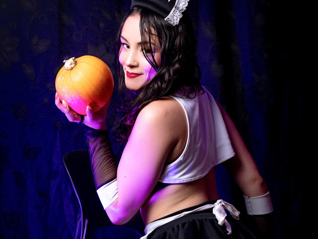 ViolettaMidnight, com cabelo preto molhado, segurando uma laranja, vestindo uma cropped branca, luvas pretas e uma tiara com laço. Posando de forma sedutora, fundo escuro, iluminação intensa em tons de roxo e azul..