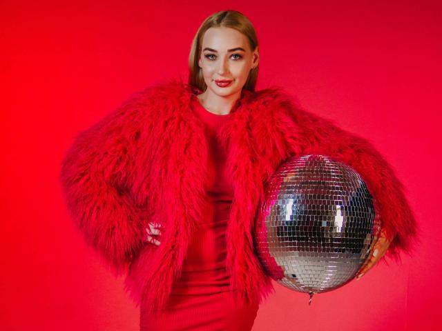 BarbaraRosy with a voluptuous figure, wearing a red fur coat over a tight red dress, holding a shiny silver disco ball. Red background, intense gaze, lips slightly parted, sexy vibe.
