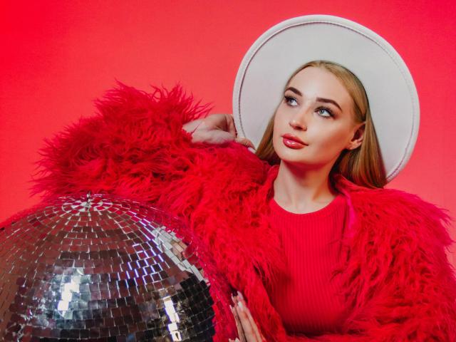 Barbara Rosy, met blond haar, een rode bontjas, een witte hoed en een rode trui, leunt tegen een glanzende zilveren discobal. helderrode achtergrond, die een intense, aantrekkelijke sfeer uitstraalt..