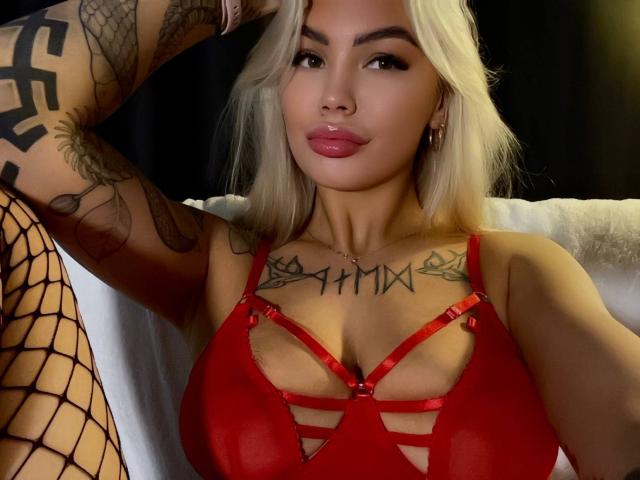 LexiLee with platinum blonde hair, red strappy lingerie, tattoos on chest and arm, fishnet stockings, plump pink lips, seductive gaze, hand behind head, sexual tension, dark background, vibrant red.