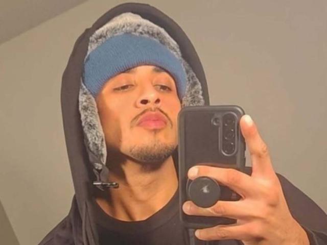 Fotografia di Xchentfoo che si scatta un selfie allo specchio con un iPhone nero. Indossa una felpa nera con un berretto blu e grigio, e guarda la telecamera con un'espressione seria..