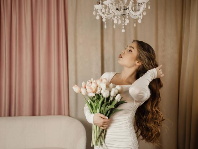 LaraPika, avec de longs cheveux bruns, une robe blanche, tenant des tulipes blanches, regardant un lustre, une main dans les cheveux, couleurs roses pastel. et des rideaux beiges en arrière-plan, pose sexy, élégant.