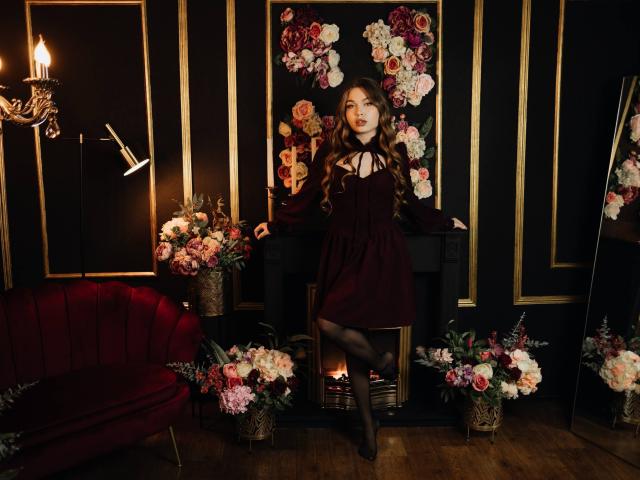 LaraPika está de pie en una habitación tenuemente iluminada, rodeada de velas y arreglos florales. Ella lleva un vestido negro, medias negras y zapatos de tacón alto rojos, irradiando un aura seductora. Increíblemente atractivo/a..