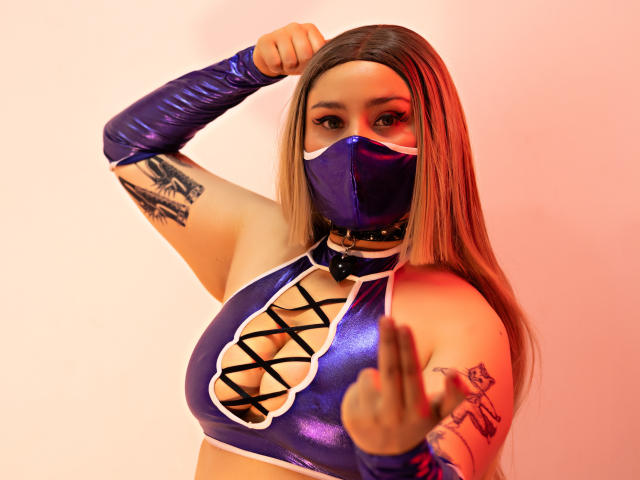 Digital artwork of DandelionQueen with long brown hair, wearing a blue, shiny, criss-crossed top, black mask, and matching glove. She's pointing forward, showing tattoos on her arm. Fucking intense gaze.