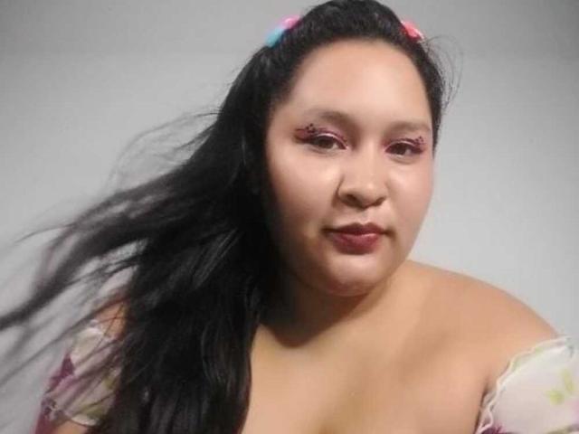 Close-up of CattaleyaBohorquez, a plus-sized Asian woman with long black hair, wearing a colorful off-shoulder top. Her hair is blowing to the left, and she's looking slightly to the right. Fucking sexy.