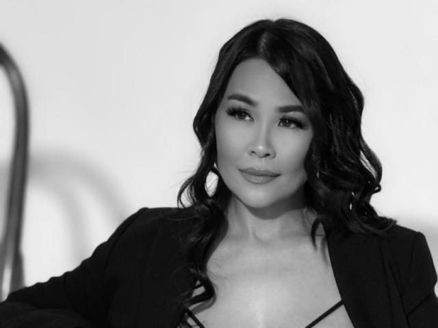 Fotografia in bianco e nero di Puiyee, una donna asiatica attraente con lunghi capelli ondulati e labbra piene, che indossa una maglietta nera. colletto leggermente aperto che lascia intravedere il décolleté, sguardo diretto verso la fotocamera.