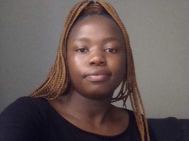 Photograph of Yollah with dark brown skin, long braided hair, and a black shirt. Yollah's face is serious, slightly smiling, with visible cheekbones and smooth skin. Fucking sexy, confident vibe.