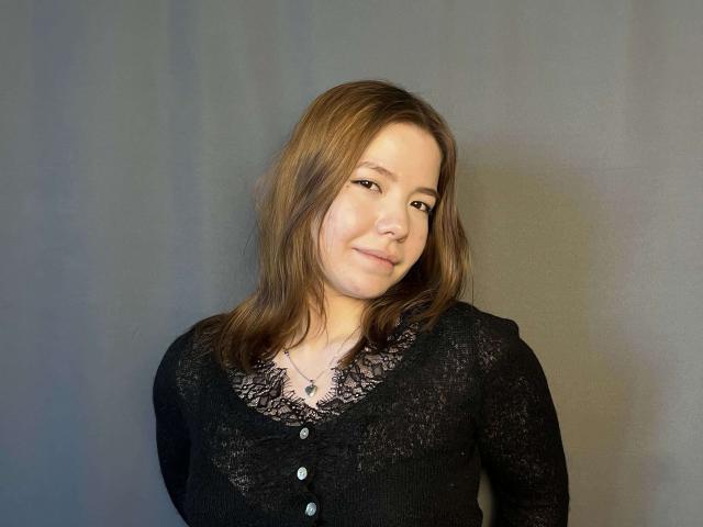 Fotografía de Nida Saltsman, de piel clara y cabello castaño, vestida con una blusa negra de encaje, mirando ligeramente hacia un lado. una sonrisa sutil. Sombras suaves a la derecha. Qué lindo..