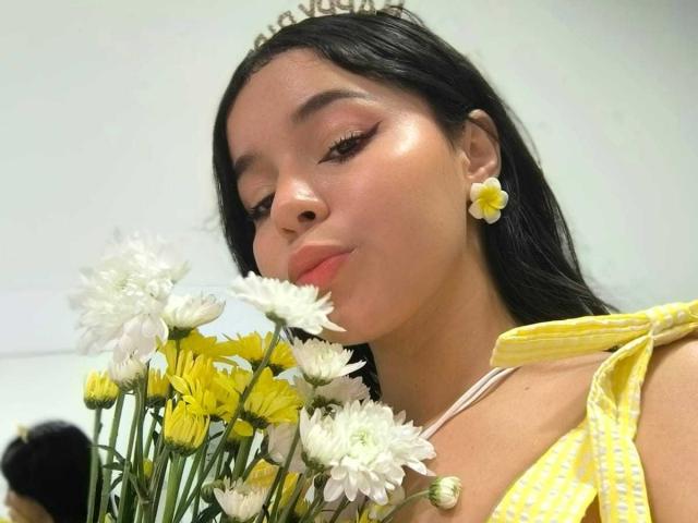 Close-up photo of LissyCarter with black hair, yellow dress, and yellow flower earrings, holding a bouquet of white and yellow daisies, eyes closed, lips slightly puckered, sexy and relaxed vibe.