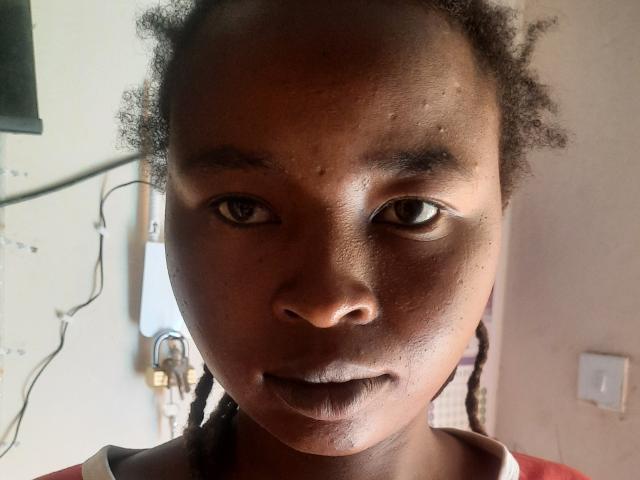 Close-up photograph of RachieChristina with dark skin, wet face, and braided hair, intense gaze, slightly parted lips, natural light from the left, shadow on the right, serious expression, high contrast.