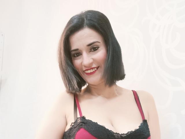 Fotografia de MaraRoberttss, uma mulher curvilínea com cabelo preto curto, batom vermelho e um sutiã vermelho com detalhes em renda preta. sorrindo diretamente para a câmera. Fundo branco. Incrivelmente atraente..
