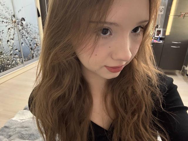 Close-up van YanDelangel met golvend bruin haar, bleke huid en rode lippen, die verleidelijk in de camera kijkt. Ze draagt een zwarte top, met subtiele sproeten op haar gezicht. Heel aantrekkelijk..