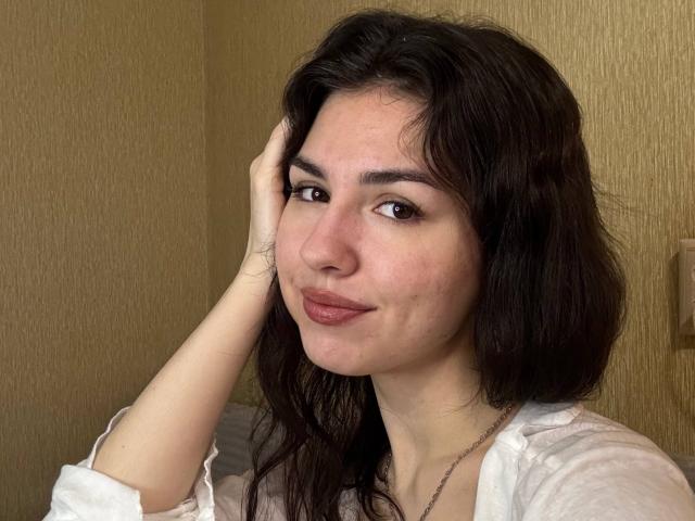 Photographie de CristieTarvin avec des cheveux bruns et ondulés, une peau claire et des yeux marrons, touchant sa tête avec une main. Elle a un léger sourire, et elle porte une chemise blanche. Il y a une tension sexuelle, elle a l'air séduisante..