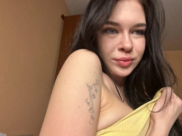 NgaKrahn a de longs cheveux foncés, une peau pâle et un tatouage sur son bras droit. Elle porte un haut jaune qui dévoile ses petites seins, et elle a un léger sourire..