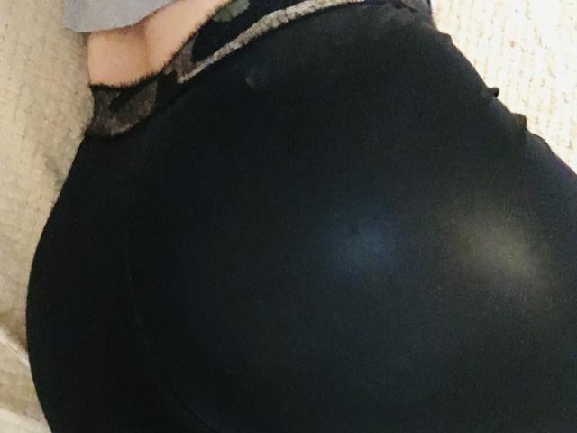 Close-up of Barbarica's ass, wearing tight black pants, with a visible white belt buckle. Her hand rests on her hip, creating a sexy, provocative pose. The lighting highlights her curves.