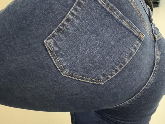 Primer plano de los glúteos de Barbarica, vestidos con unos vaqueros azules ajustados, que resaltan la curva y el bolsillo trasero. La tela vaquera está ligeramente desgastada y tiene costuras visibles. Las caderas de Barbarica están juntas..