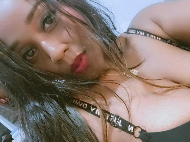 Close-up of Yirily with wet, disheveled brown hair, red lipstick, and black strappy top showing cleavage. Glossy skin, seductive gaze, slight smile. Visible nipple outline, sexual tension. Slightly messy look.