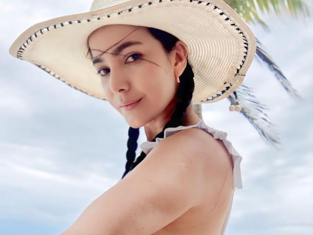 Primo piano di BellaVelvet, una donna asiatica con la pelle chiara, i capelli neri intrecciati e un cappello di paglia bianca con bordi neri. Si sta guardando indietro, sorridendo leggermente. La sua maglietta è a spalle scoperte..