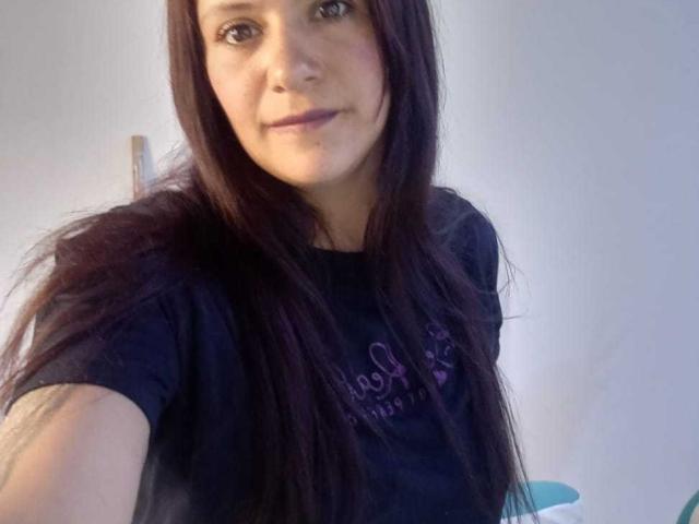 Close-up photo of AriannaSeete, a young woman with long, straight black hair, wearing a black t-shirt, smiling slightly. Soft natural light highlights her face and hair, creating a casual, relaxed vibe.