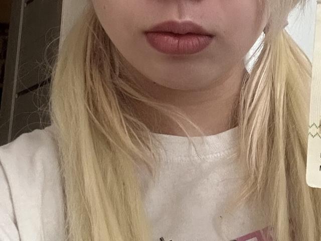 Close-up of JeanaLamonte's face, showing her full lips with dark red lipstick. She has blonde hair, slightly messy, wearing a white shirt. The lighting highlights her facial features and lips.