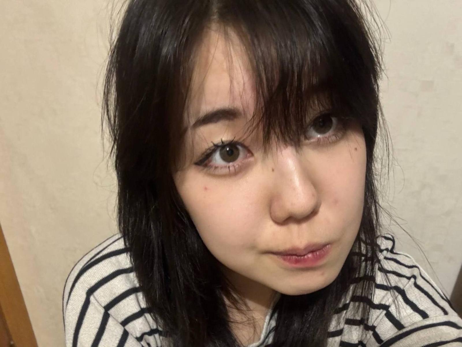 Primo piano di Andrea Achekian, una donna asiatica con la pelle chiara, capelli neri e piccole lentiggini sulle guance. Indossa una camicia a righe bianche e nere, e guarda direttamente l'obiettivo con un sorriso appena accennato. I suoi occhi sono grandi e scuri, e le sue labbra sono leggermente socchiuse..