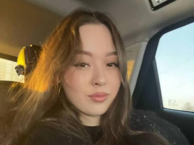 Autoportrait en gros plan de MikeBooras, une jeune femme à la peau claire et aux longs cheveux bruns, assise dans une voiture, regardant directement la caméra. La photo, prise avec une légère moue, avec une lumière naturelle douce..