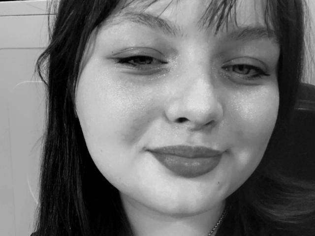 Close-up black and white photograph of MollyLolly-hot, face centered, wet skin glistening, dark straight hair with bangs, subtle smile, dark lips, slightly glossy eyes, visible droplets on face.