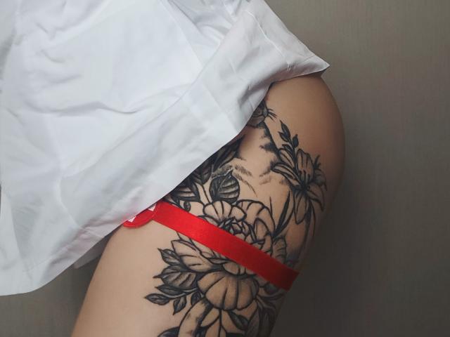 Primo piano dell'anca e della coscia di Niferttiti, che mostra un grande tatuaggio floreale nero, uno slip rosso e una camicia bianca. I dettagli del tatuaggio sono complessi, con rose e foglie. La pelle è chiara.
.
