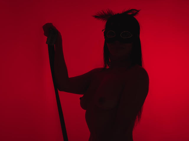 Silhouette of HelenHard against a bright red background, holding a staff with her right hand. She has long hair and a wild hairstyle on top. Fucking intense red glow.