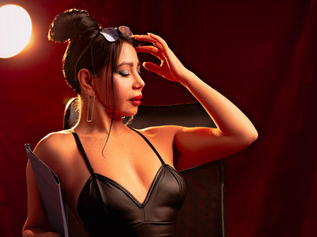 Digital artwork of HelenHard, a sexy woman with dark hair in a bun, wearing a black strapless top, adjusting her sunglasses with a seductive, confident gaze. Bright red lighting, intense shadows.