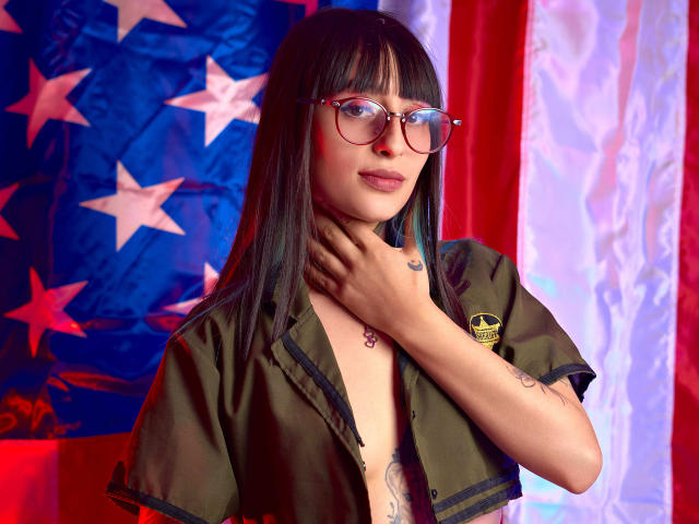 TatsumiLee, com cabelo preto longo e óculos, vestindo uma camisa aberta estilo militar, com a mão no pescoço, e uma bandeira americana. estrelas e listras ao fundo, cores vibrantes, tensão sexual, pose sedutora..