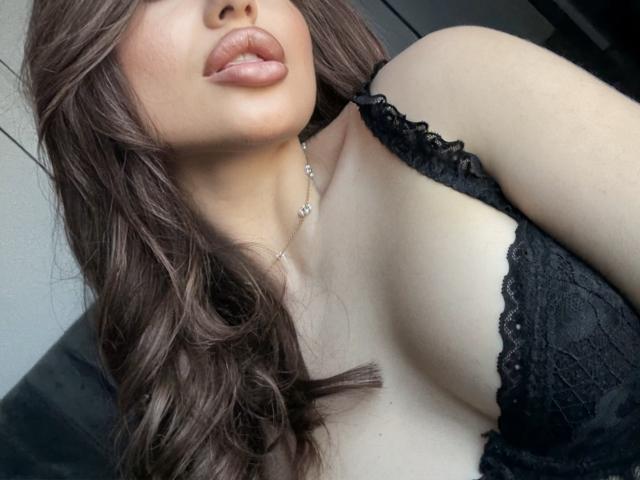 Close-up photo of DenissaAnessa, her lips slightly parted, wearing black lace lingerie, exposing cleavage, her brown wavy hair partially covering her face, wearing a delicate necklace. Fucking sexy.