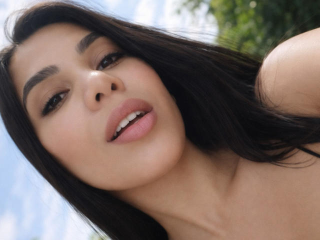 Photo en gros plan d'AnnyFriend, une femme avec de longs cheveux noirs, des lèvres pulpeuses et des sourcils foncés, regardant directement l'appareil photo. avec la bouche légèrement ouverte. Une lumière naturelle et douce illumine son visage..