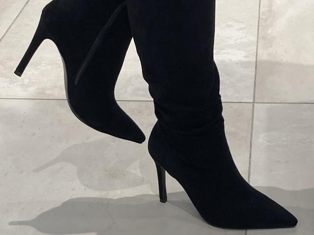 Silhouette des jambes de DeesseBleue, vêtue d'un pantalon noir moulant et de bottes noires à talons hauts, projetant des ombres sur un fond lumineux. Sol en carreaux blancs.
les bottes ont une pointe effilée et un talon aiguille haut..